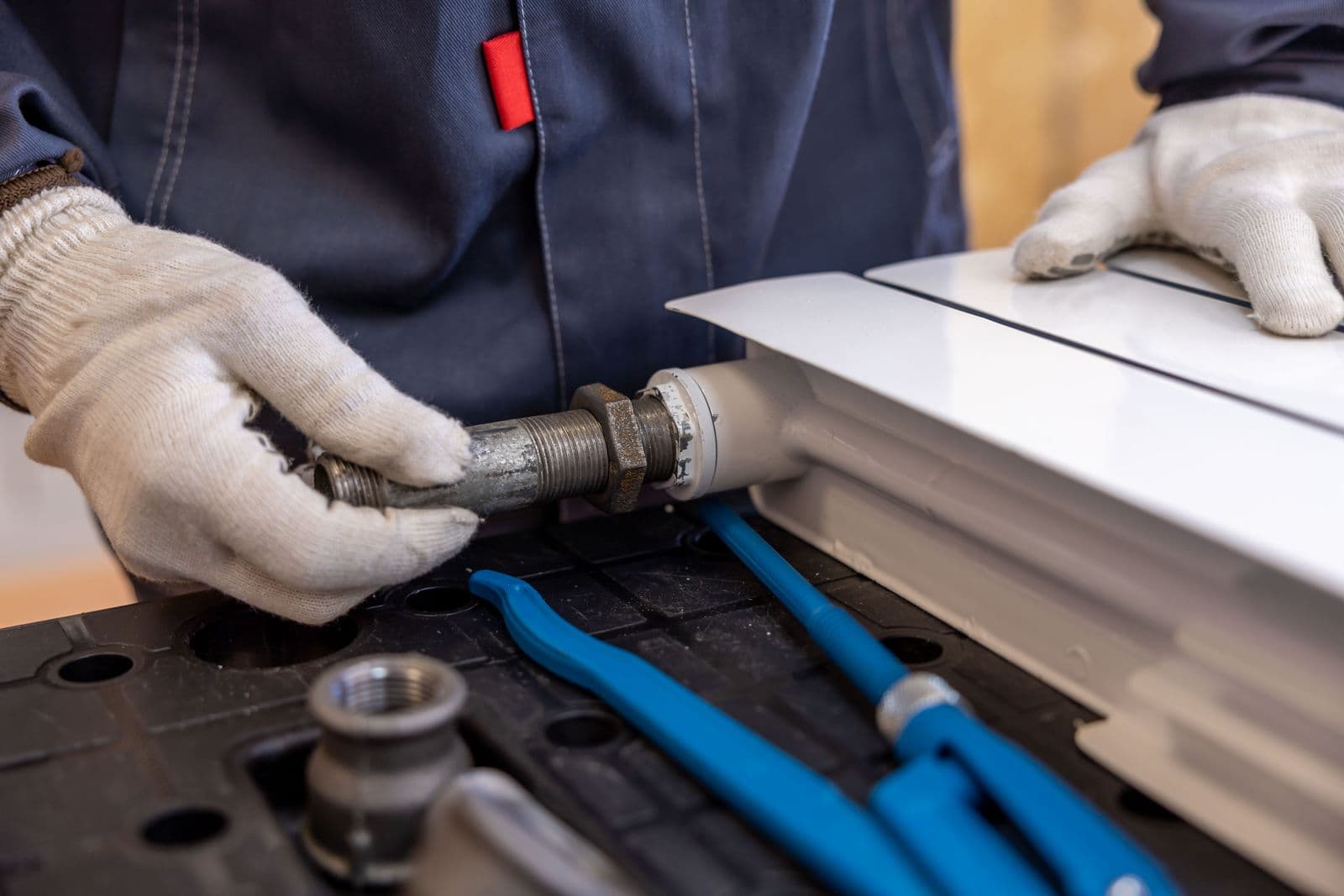 Uniformed plumber tightening a threaded pipe fitting with a wrench